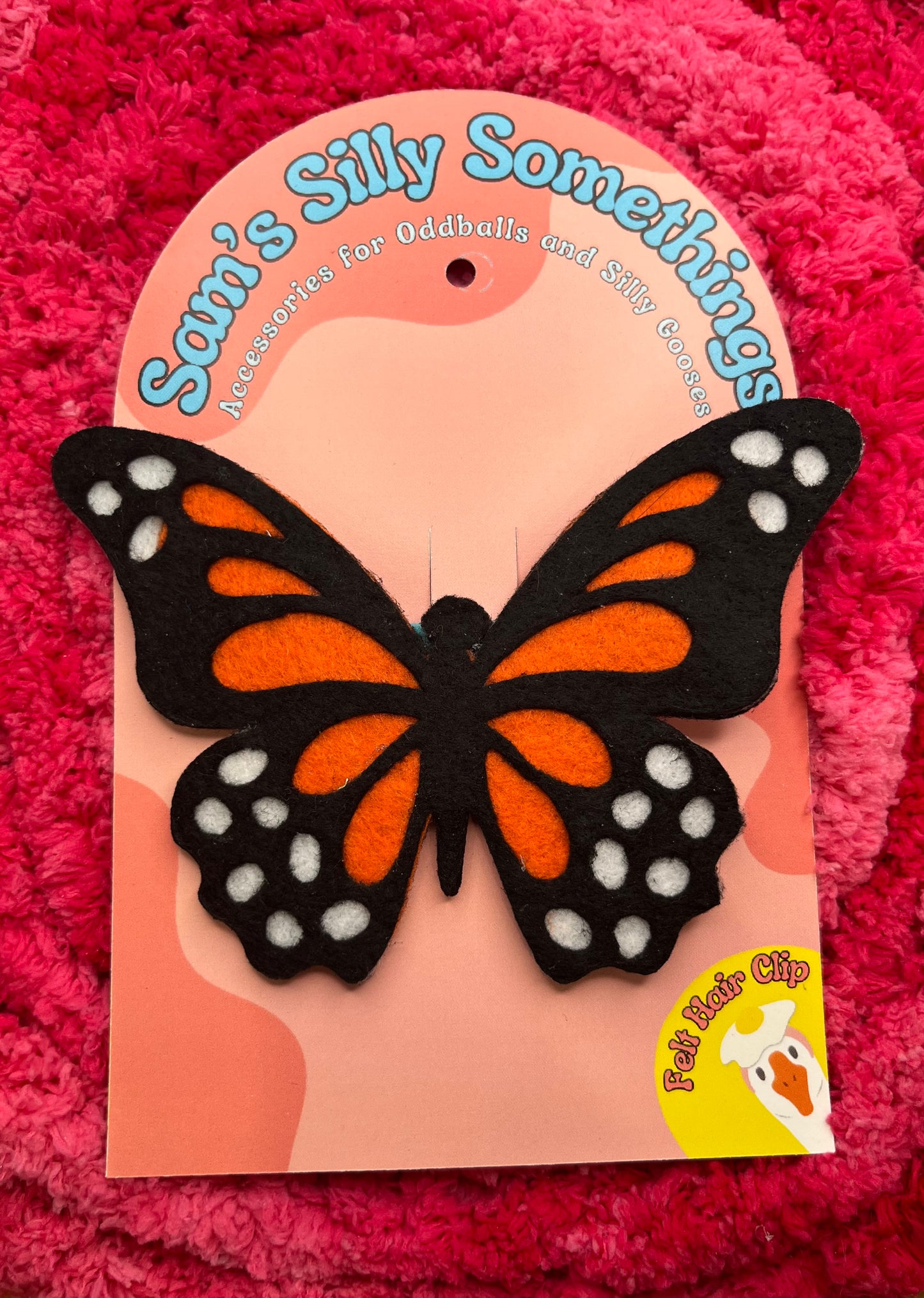 Butterfly hair clip packaging with 'Sam's Silly Somethings' branding on a pink textured background.