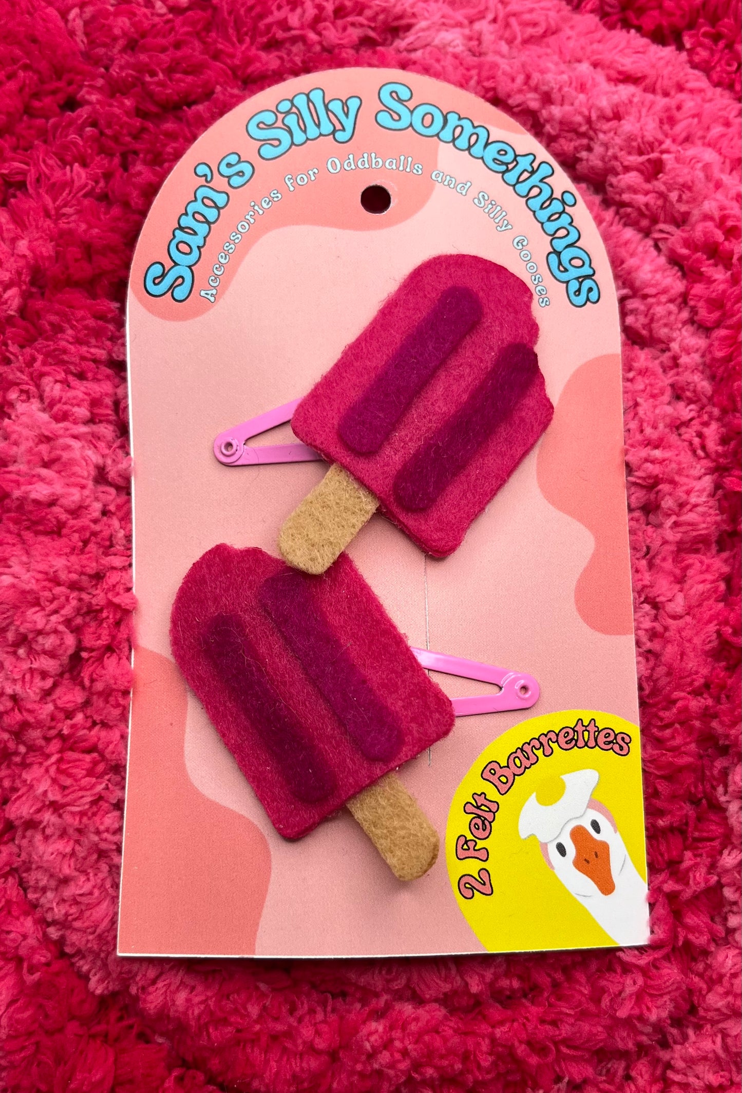Packaged hair accessories shaped like popsicles on a pink textured background