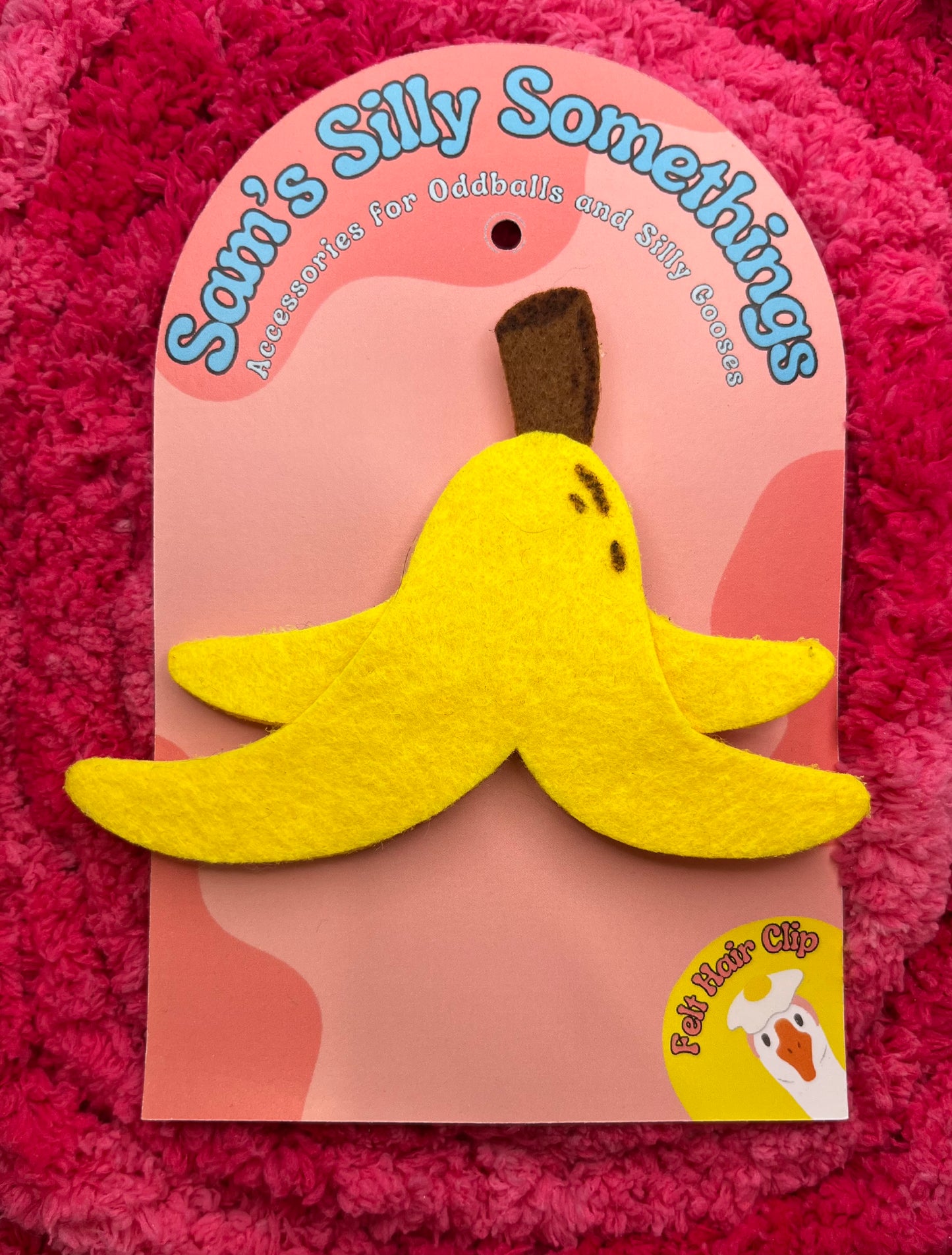Hair clip with a banana design on a pink card with 'Sam's Silly Somethings' text, on a pink textured background.