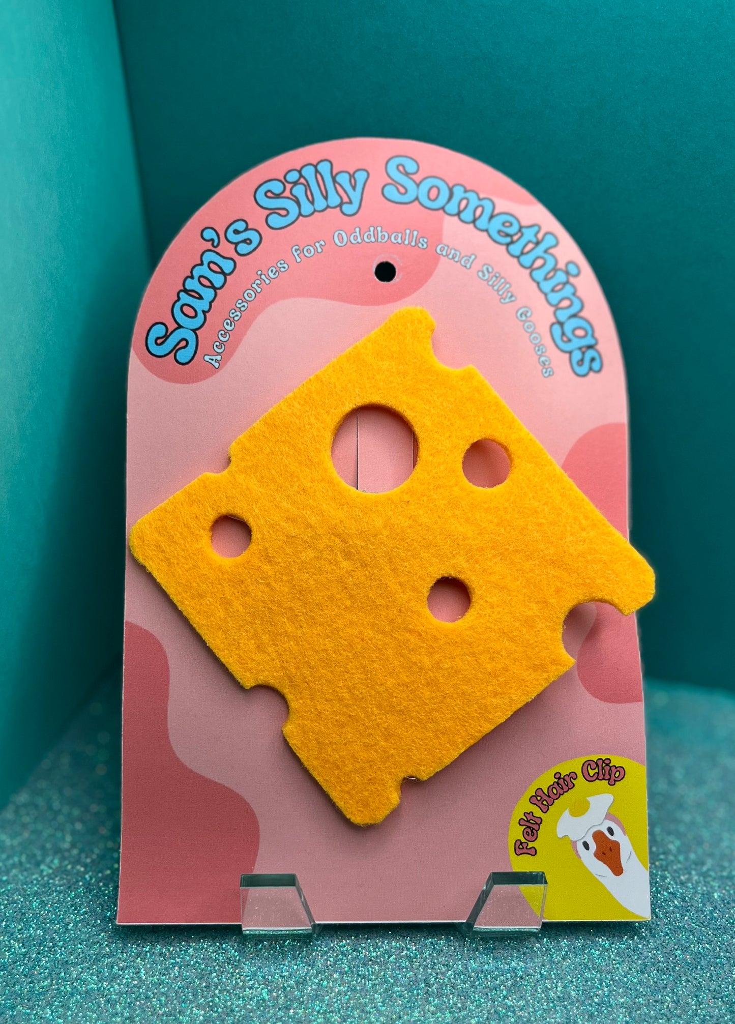 Yellow cheese-shaped hair clip on a pink packaging with 'Sam's Silly Somethings' branding.
