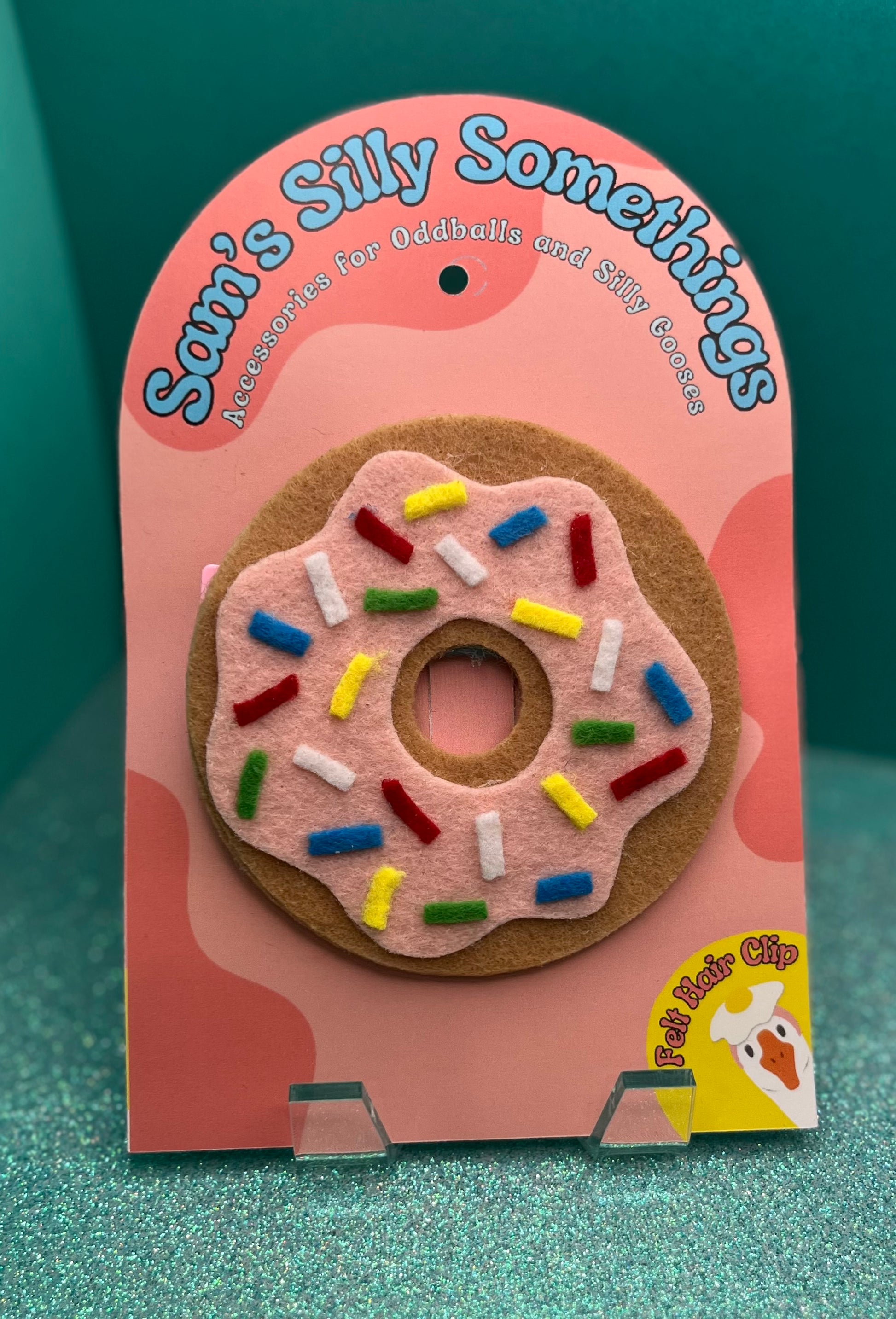 Donut-shaped hair clip with colorful sprinkles on a pink label with 'Sam's Silly Somethings' text.