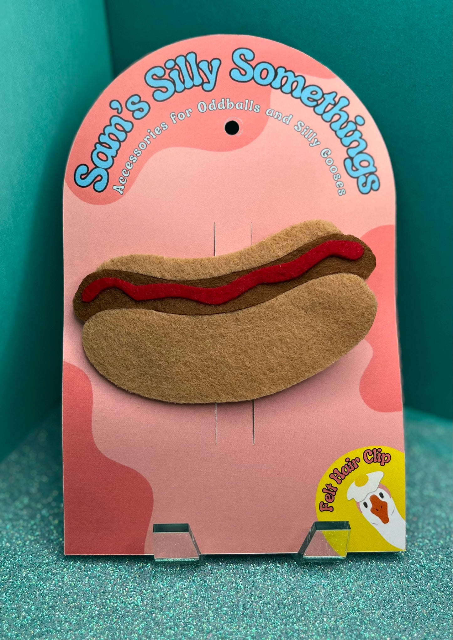 Hot dog-shaped hair clip on a pink card with 'Sam's Silly Somethings' branding.