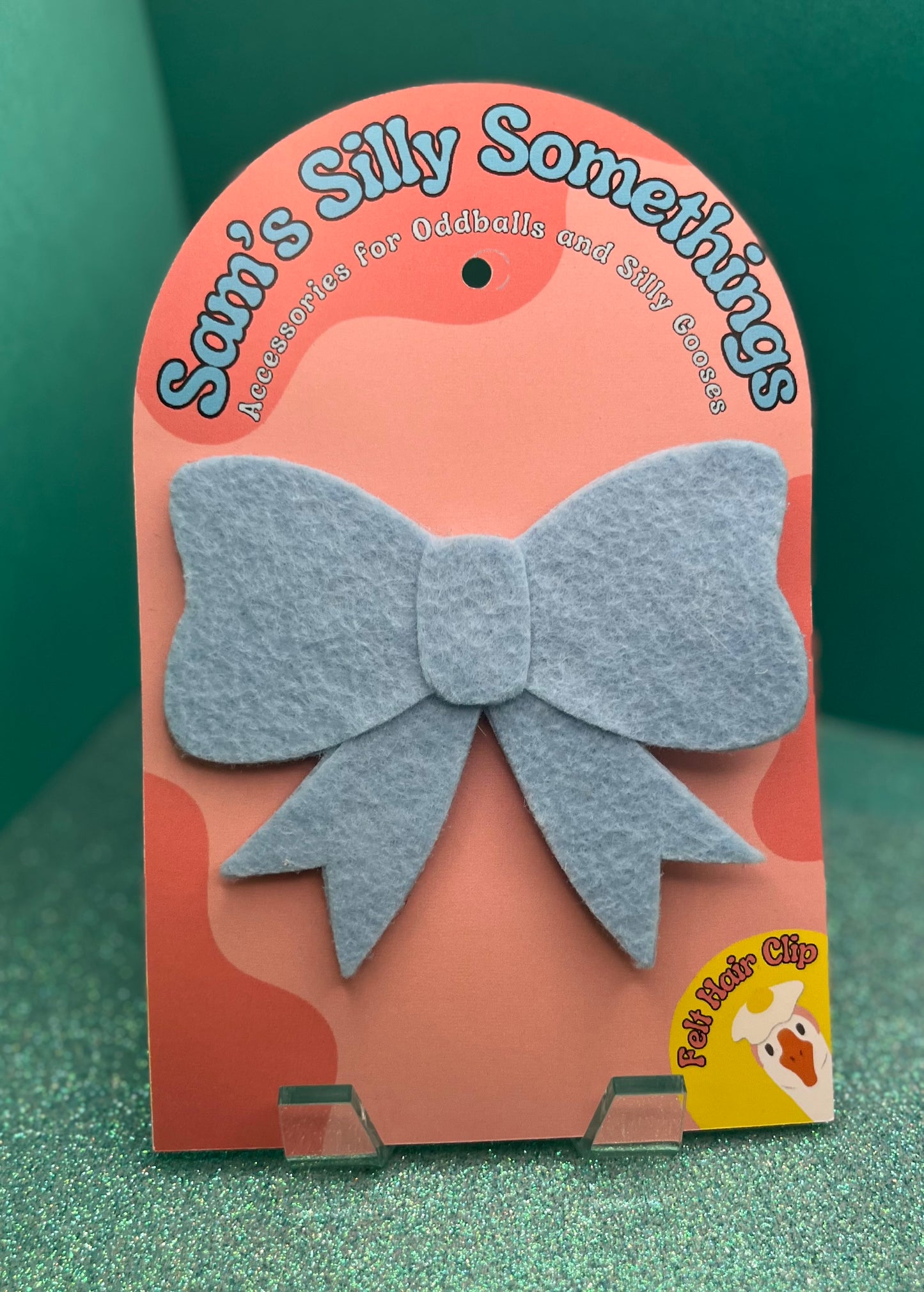 Blue bow hair clip on a pink packaging with 'Sam's Silly Somethings' branding.