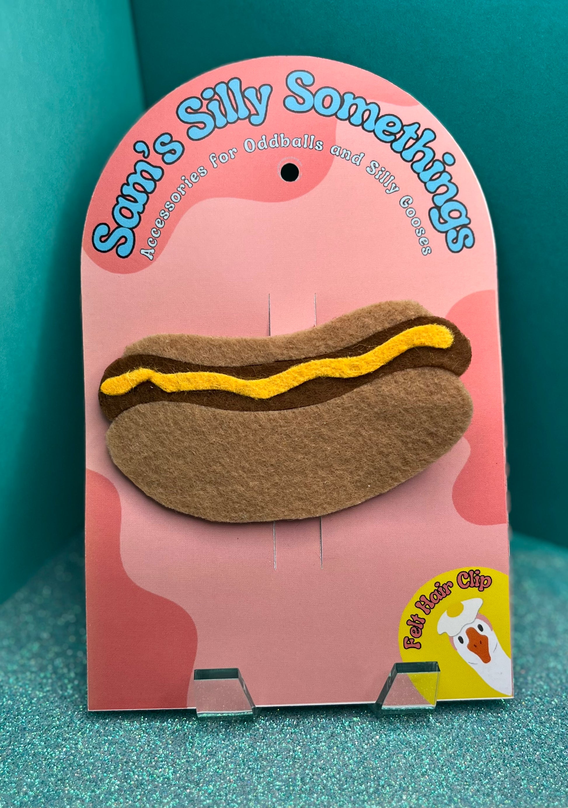 Hot dog-shaped hair clip on a pink packaging with 'Sam's Silly Somethings' branding.
