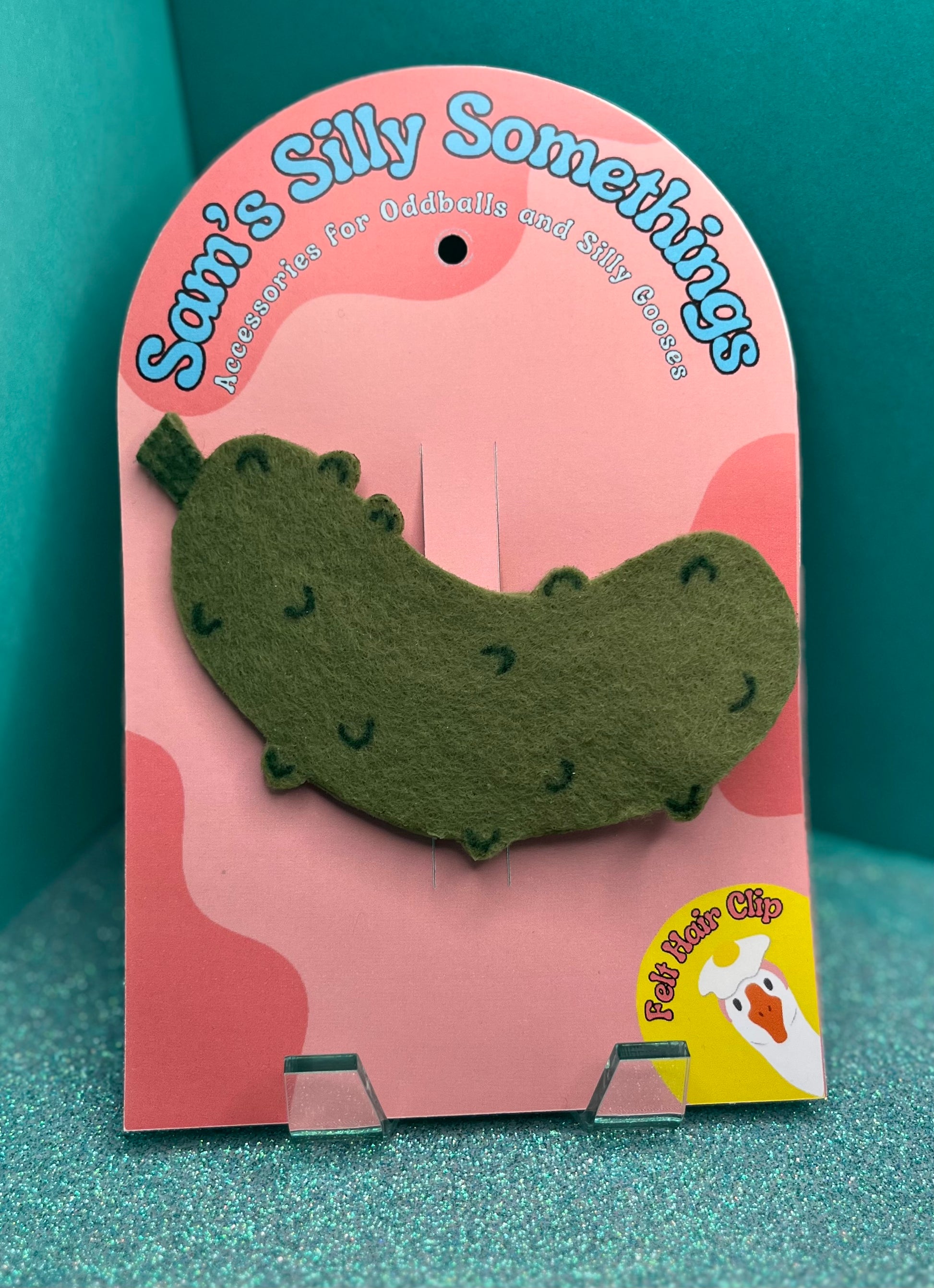 Green pickle-shaped hair clip on a pink card with 'Sam's Silly Somethings' branding.
