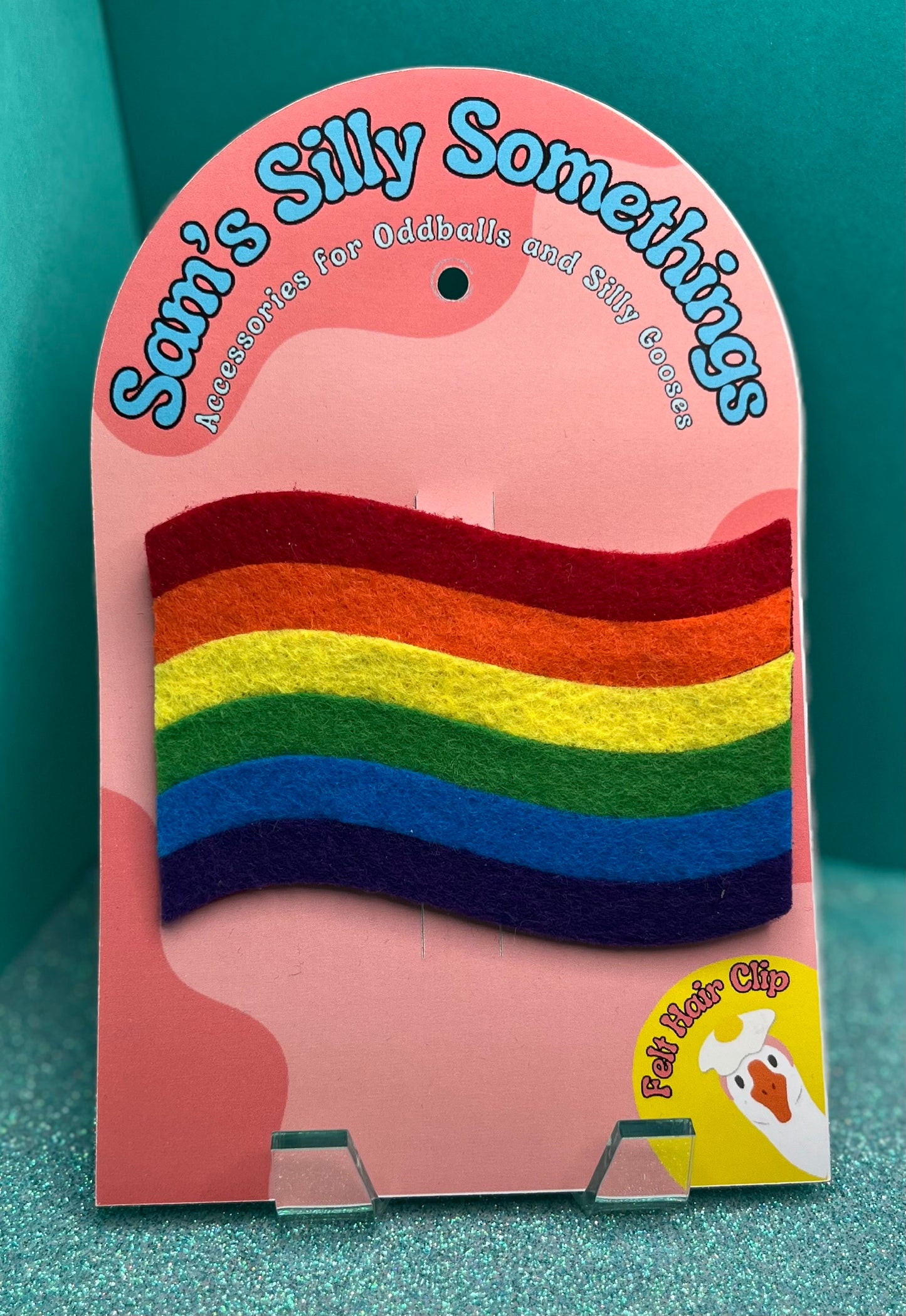 Packaged rainbow hair clip with 'Sam's Silly Somethings' branding on a teal background