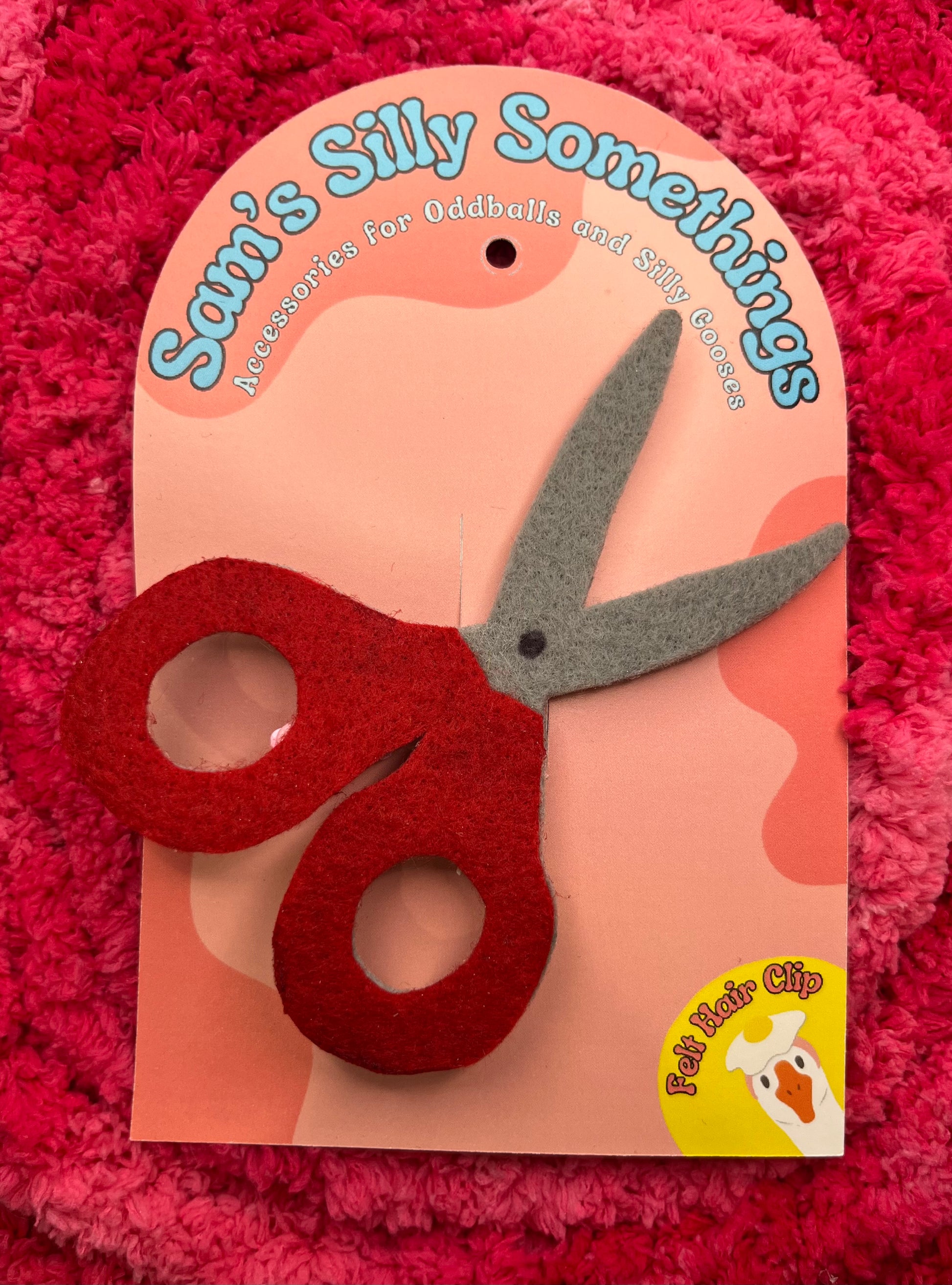 Red scissors on a pink card with 'Sam's Silly Somethings' branding on a red textured background.