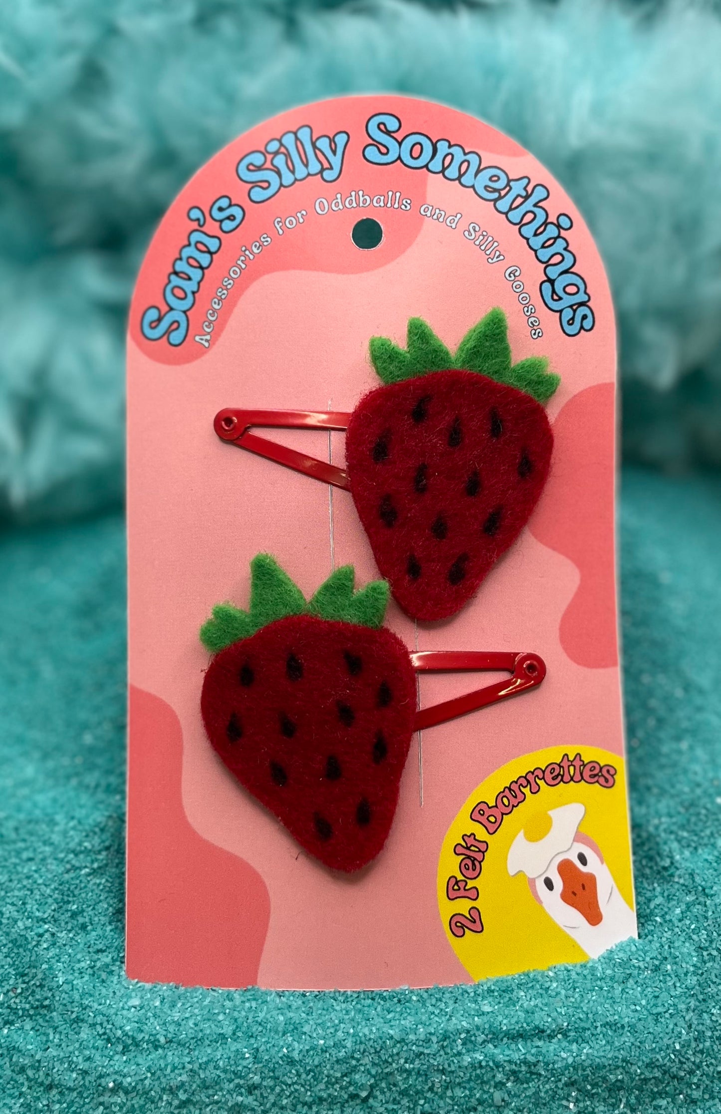 Two red strawberry-shaped polyester felt barrettes with green accents, attached to a pink card with the text 'Sam's Silly Somethings'.